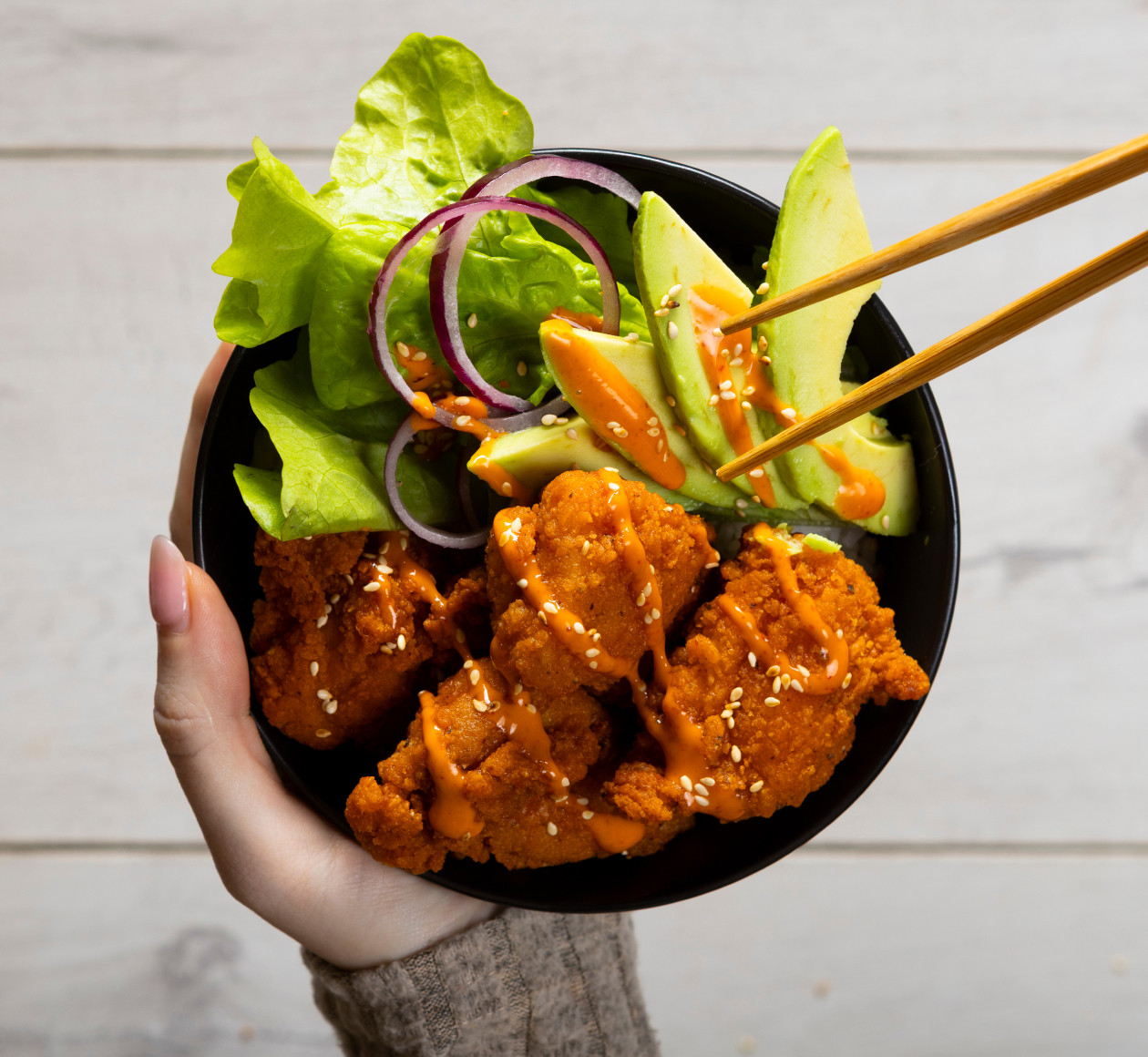 Hand holding a bowl of Machi ready-to-cook chicken with fresh salad